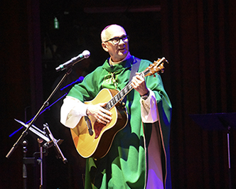 Bishop Joseph holding a guitar and singing at a microphone